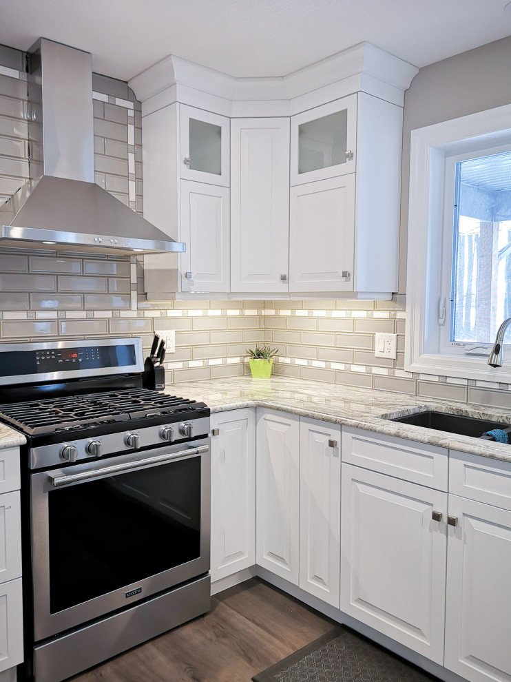 Example of a mid-sized transitional u-shaped light wood floor and brown floor enclosed kitchen design in Toronto with an undermount sink, raised-panel cabinets, white cabinets, granite countertops, beige backsplash, glass tile backsplash, stainless steel appliances, a peninsula and gray countertops