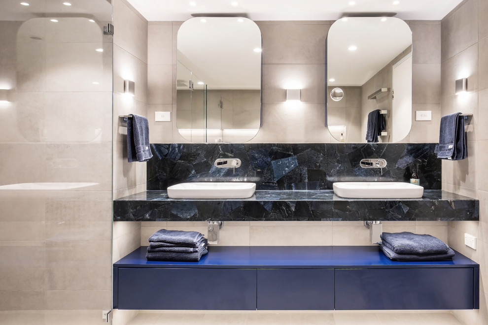 This is an example of a mid-sized contemporary master bathroom in Sydney with flat-panel cabinets, blue cabinets, an alcove shower, a wall-mount toilet, beige tile, porcelain tile, beige walls, porcelain floors, a vessel sink, beige floor, a hinged shower door, blue benchtops, a niche, a double vanity and a floating vanity.