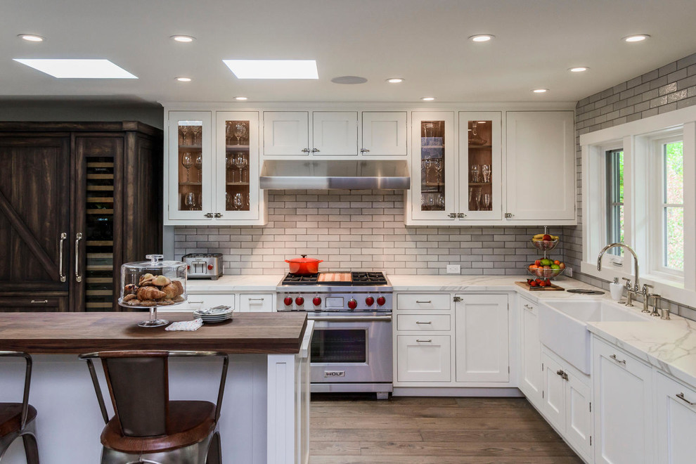 Inspiration for a large transitional l-shaped kitchen in San Francisco with a farmhouse sink, shaker cabinets, white cabinets, dark hardwood floors, grey splashback, subway tile splashback, stainless steel appliances and with island.
