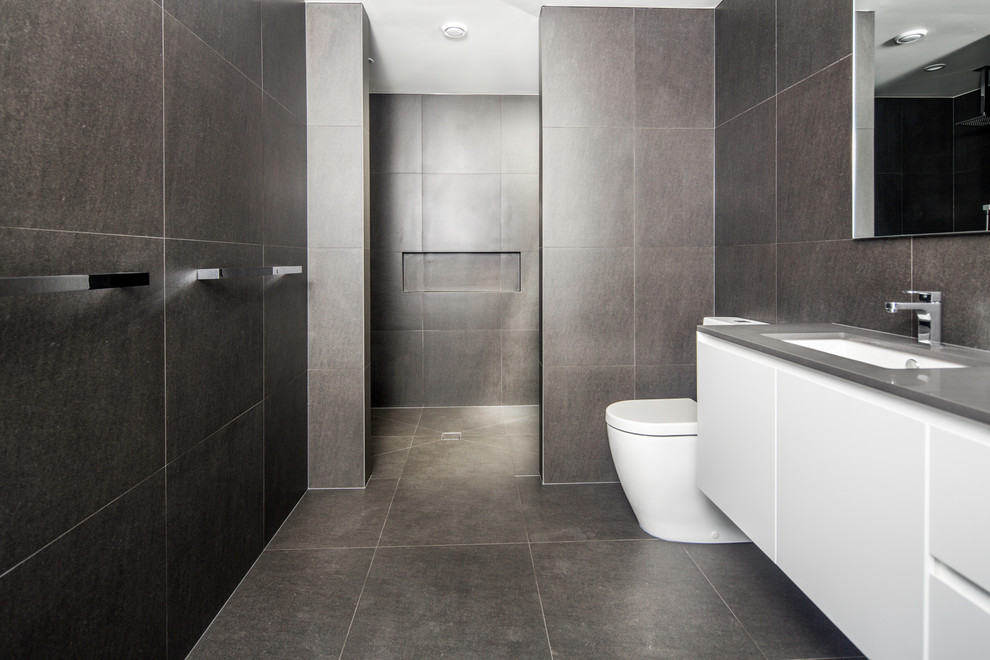 Photo of a large contemporary master bathroom in Brisbane with flat-panel cabinets, white cabinets, a freestanding tub, a double shower, a one-piece toilet, gray tile, porcelain tile, grey walls, porcelain floors, an undermount sink, engineered quartz benchtops, grey floor, an open shower and grey benchtops.
