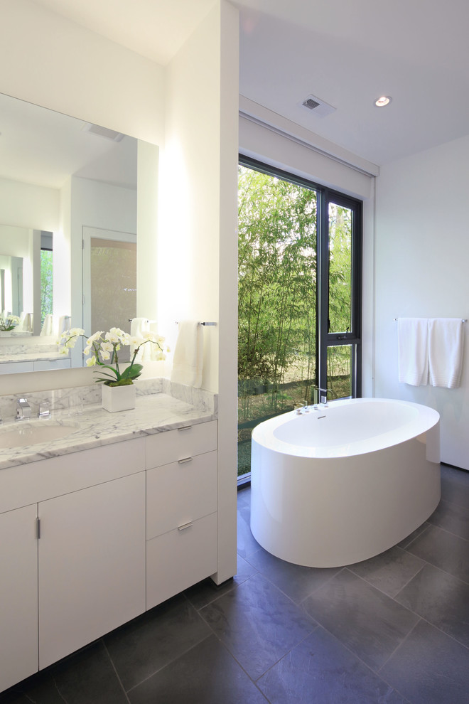 Inspiration for a modern bathroom in Raleigh with an undermount sink, flat-panel cabinets, white cabinets, a freestanding tub, white walls and slate floors.