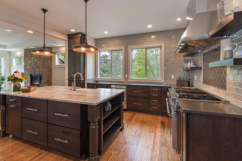 Open concept kitchen - large transitional l-shaped medium tone wood floor and brown floor open concept kitchen idea with a farmhouse sink, shaker cabinets, dark wood cabinets, granite countertops, gray backsplash, subway tile backsplash, paneled appliances and an island