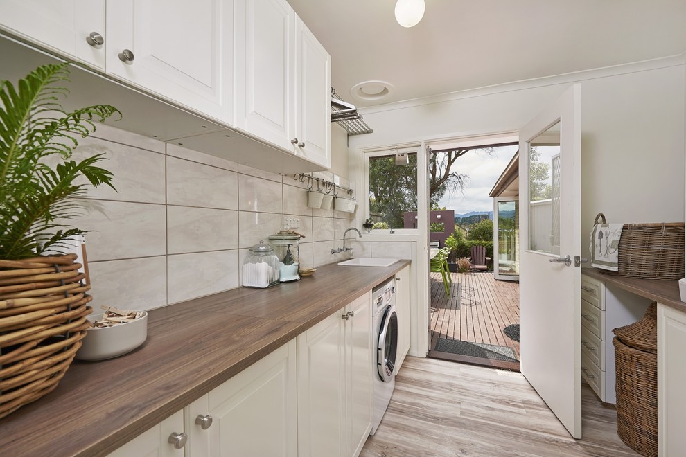 Design ideas for a mid-sized transitional galley dedicated laundry room in Melbourne with a drop-in sink, shaker cabinets, white cabinets, laminate benchtops and white walls.