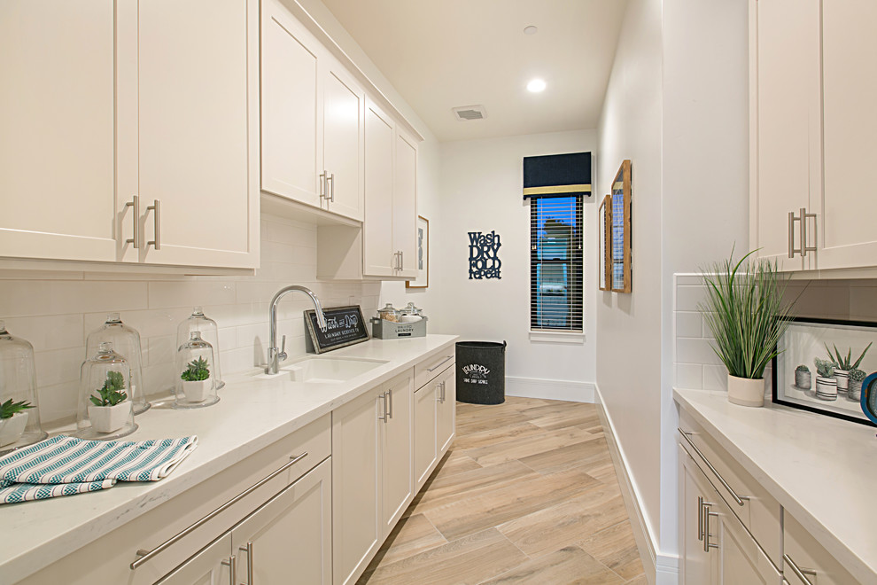 Large country galley laundry room in San Diego with an integrated sink, recessed-panel cabinets, white cabinets, quartz benchtops, white walls, porcelain floors, a side-by-side washer and dryer, beige floor and white benchtop.
