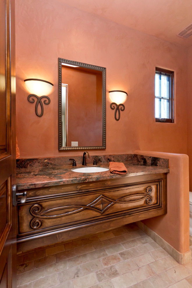 Design ideas for a mid-sized mediterranean powder room in Phoenix with an undermount sink, medium wood cabinets, granite benchtops, a one-piece toilet, pink walls and travertine floors.