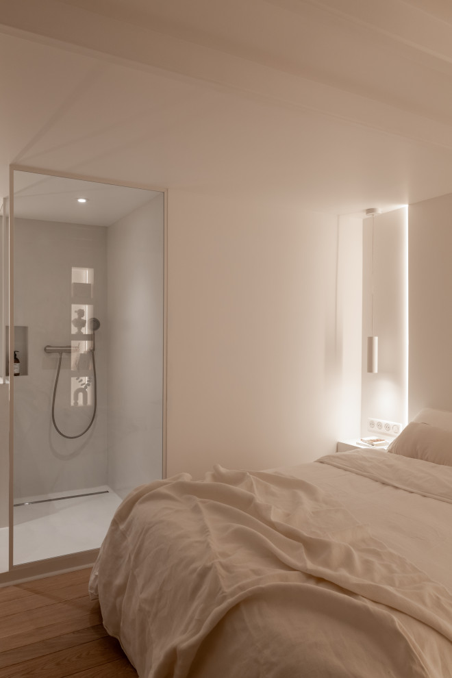 Modelo de habitación de invitados beige y blanca actual de tamaño medio sin chimenea con paredes blancas, suelo de madera clara y suelo marrón