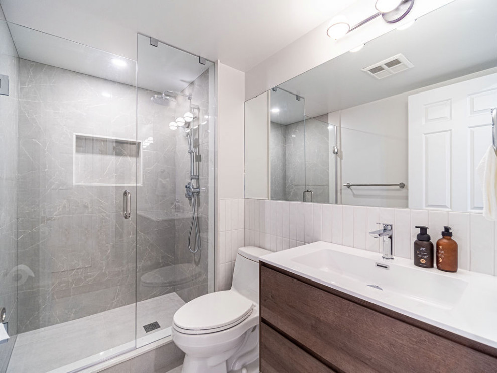 Photo of a small modern family bathroom in Toronto with flat-panel cabinets, medium wood cabinets, a one-piece toilet, white tiles, ceramic tiles, white walls, ceramic flooring, an integrated sink, grey floors, a hinged door, white worktops, a single sink, a floating vanity unit and an alcove shower.
