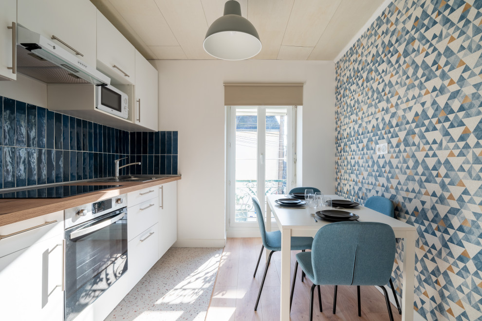 This is an example of a mid-sized contemporary single-wall open plan kitchen in Nantes with an undermount sink, white cabinets, wood benchtops, blue splashback, ceramic splashback, panelled appliances, linoleum floors, multi-coloured floor and beige benchtop.