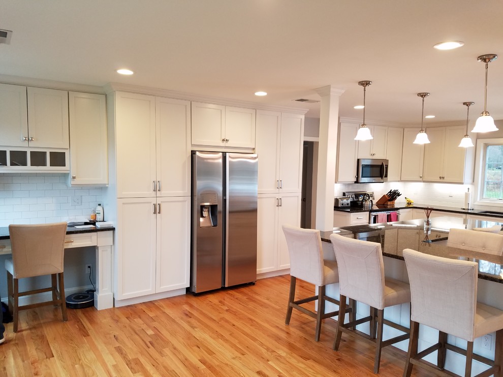 Large transitional l-shaped light wood floor and brown floor eat-in kitchen photo with an undermount sink, shaker cabinets, white cabinets, granite countertops, white backsplash, subway tile backsplash, stainless steel appliances and an island