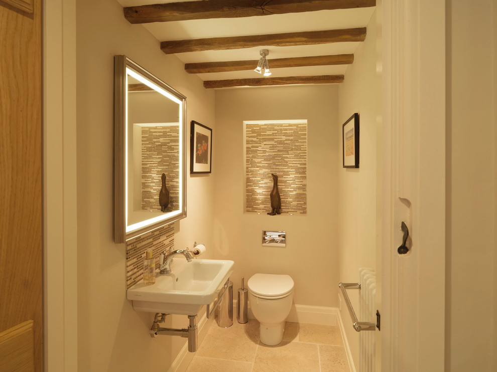 Photo of a small country powder room in Hampshire with a wall-mount sink, beige walls, a one-piece toilet, beige tile, glass tile and limestone floors.