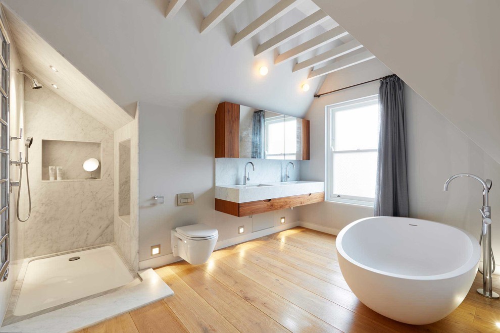 Design ideas for a large contemporary master bathroom in London with medium wood cabinets, a freestanding tub, an open shower, a wall-mount toilet, stone slab, marble benchtops, flat-panel cabinets, white walls, medium hardwood floors, an undermount sink and an open shower.