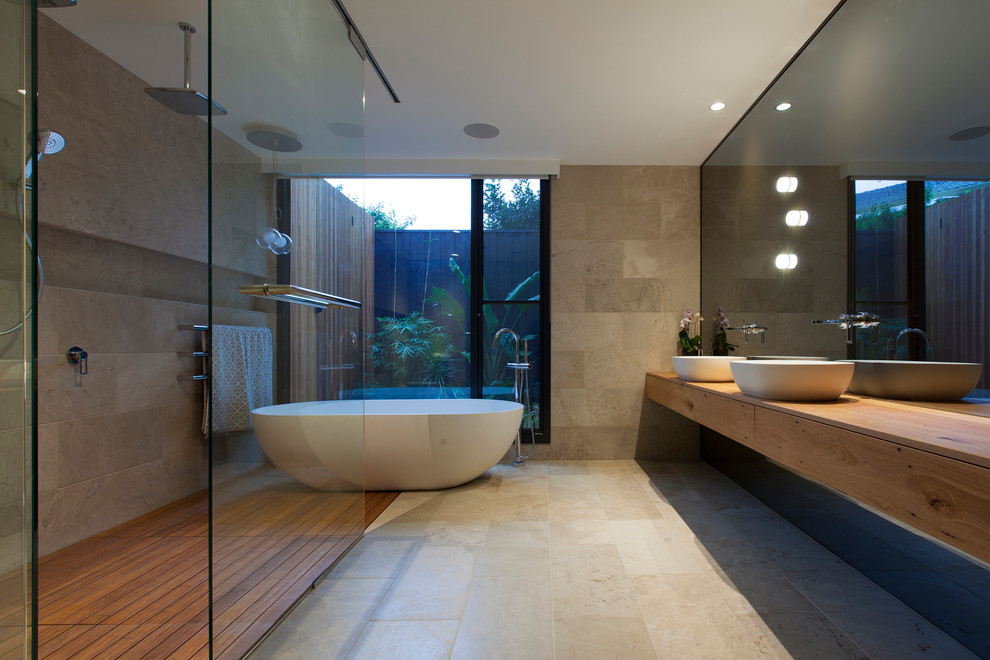 This is an example of a contemporary master bathroom in Melbourne with medium wood cabinets, a freestanding tub, an open shower, stone tile, a vessel sink and an open shower.