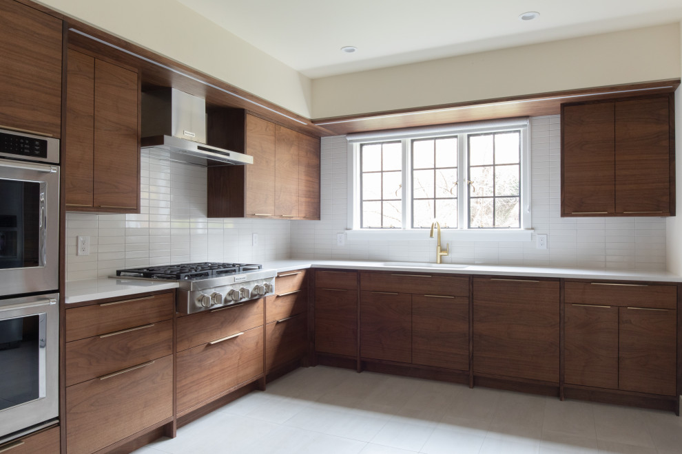 Large midcentury l-shaped kitchen in New York with an undermount sink, flat-panel cabinets, dark wood cabinets, white splashback, subway tile splashback, stainless steel appliances, porcelain floors, no island, white floor and white benchtop.