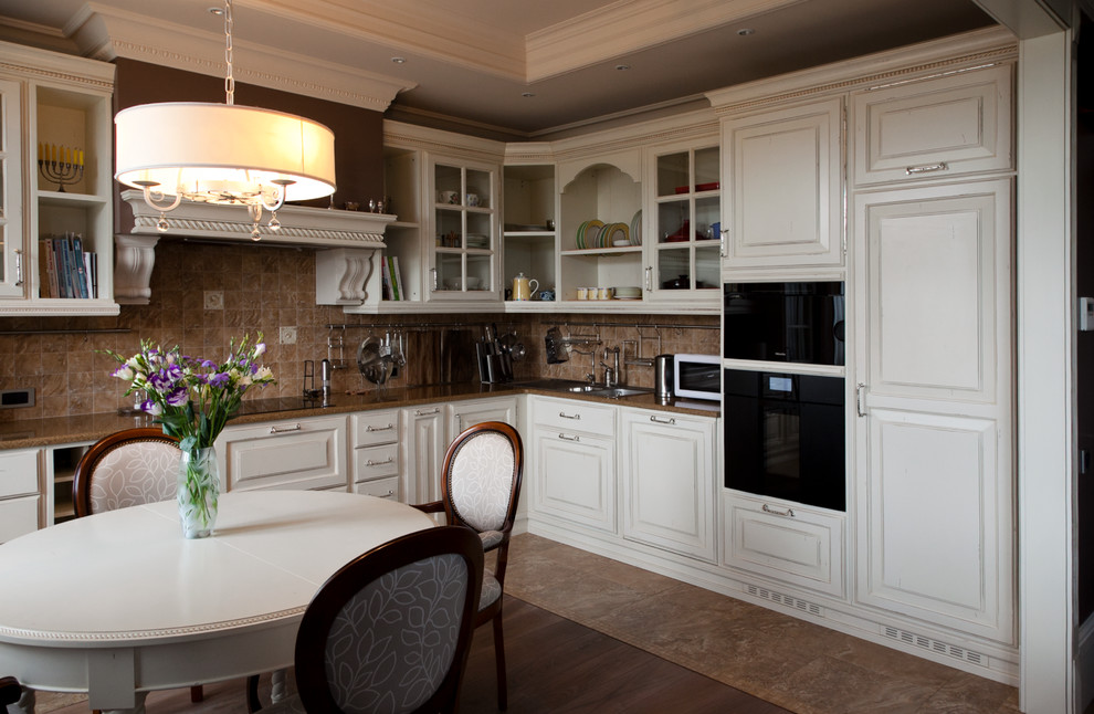 This is an example of a mid-sized traditional l-shaped eat-in kitchen in Moscow with white cabinets, brown splashback, no island, an undermount sink, raised-panel cabinets and black appliances.