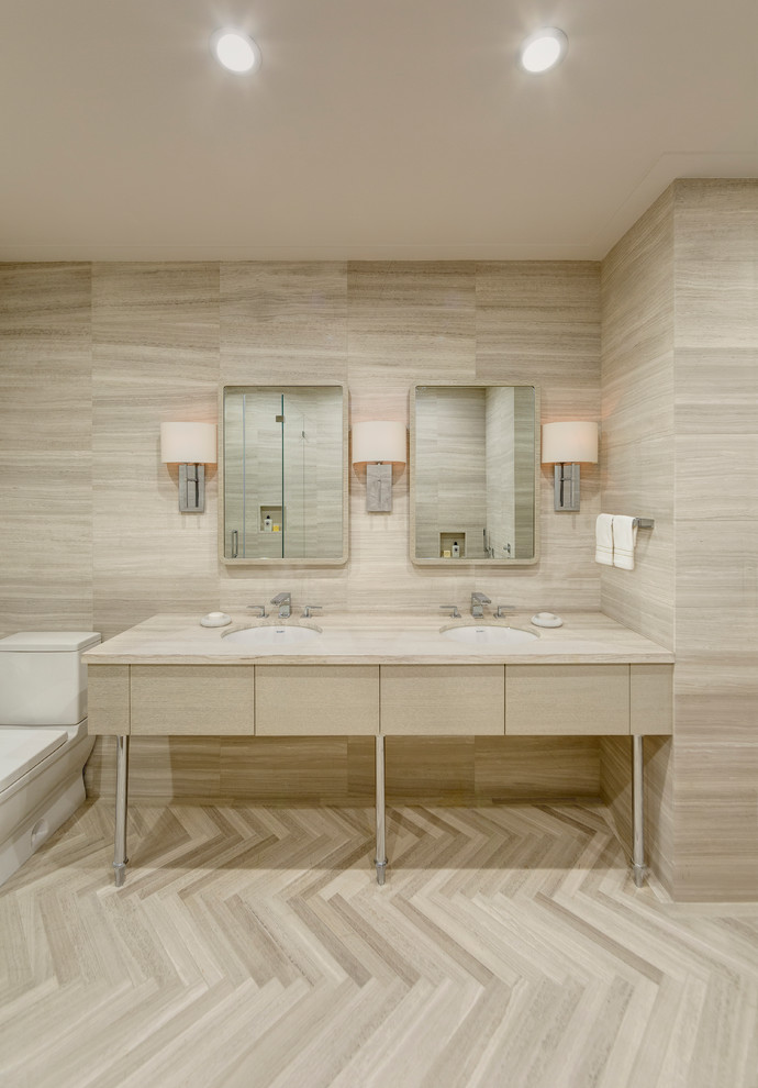 This is an example of a large contemporary master bathroom in New York with an undermount sink, flat-panel cabinets, light wood cabinets, limestone benchtops, a freestanding tub, a corner shower, a one-piece toilet, brown tile, stone tile, brown walls and limestone floors.