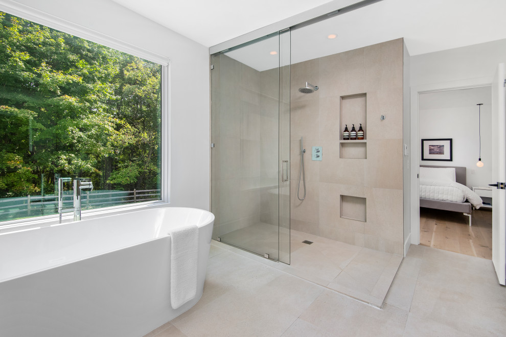 This is an example of a modern master bathroom with open cabinets, light wood cabinets, a freestanding tub, a curbless shower, a one-piece toilet, gray tile, white walls, beige floor, a sliding shower screen and white benchtops.