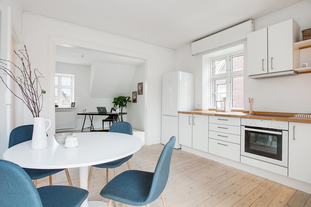 This is an example of a mid-sized scandinavian single-wall eat-in kitchen in Copenhagen with flat-panel cabinets, white cabinets, wood benchtops, white appliances, light hardwood floors and no island.
