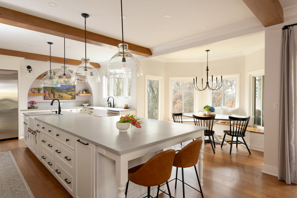 Example of a large medium tone wood floor and exposed beam eat-in kitchen design with white backsplash, stainless steel appliances and an island