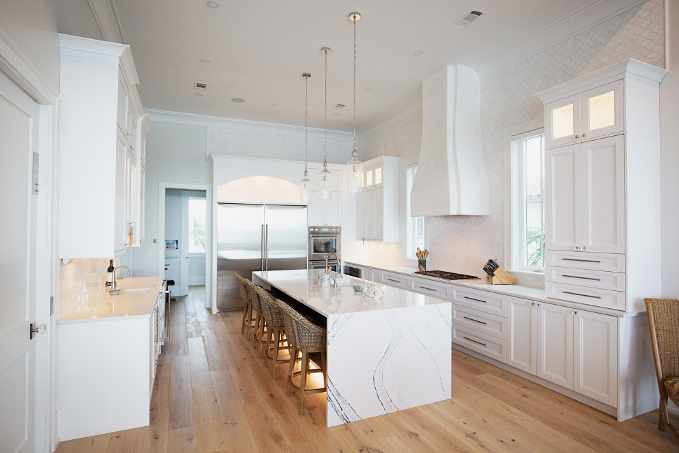 This is an example of an expansive nautical l-shaped kitchen/diner in Miami with a built-in sink, shaker cabinets, white cabinets, quartz worktops, white splashback, ceramic splashback, stainless steel appliances, medium hardwood flooring, an island, beige floors and white worktops.
