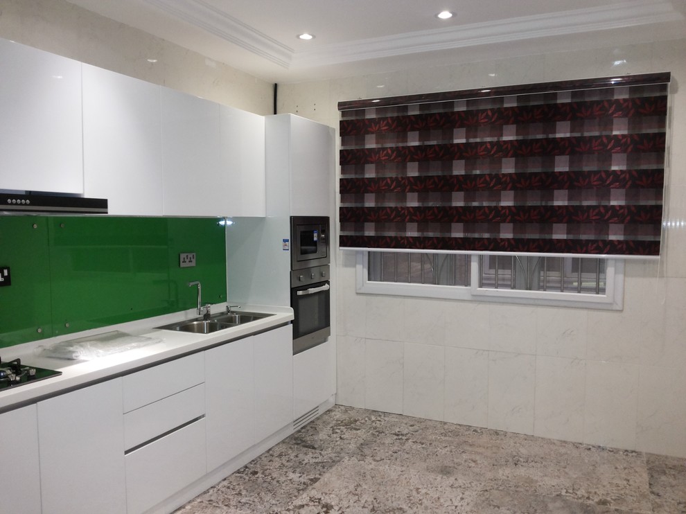Design ideas for a modern single-wall separate kitchen in Other with an undermount sink, flat-panel cabinets, white cabinets, solid surface benchtops, green splashback, glass tile splashback, stainless steel appliances and no island.
