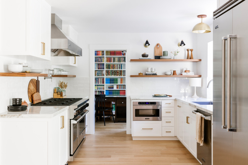 Example of a mid-sized transitional u-shaped light wood floor and beige floor kitchen design in San Francisco with an undermount sink, shaker cabinets, white cabinets, white backsplash, ceramic backsplash, stainless steel appliances, no island and white countertops