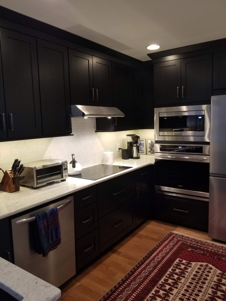 Modern inredning av ett avskilt, litet vit vitt l-kök, med en undermonterad diskho, skåp i shakerstil, svarta skåp, bänkskiva i kvarts, vitt stänkskydd, stänkskydd i porslinskakel, rostfria vitvaror, ljust trägolv, en halv köksö och svart golv
