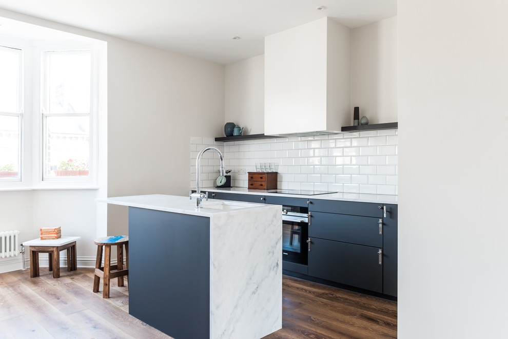 Photo of a small scandinavian u-shaped open plan kitchen in London with a drop-in sink, recessed-panel cabinets, black cabinets, marble benchtops, white splashback, cement tile splashback, stainless steel appliances, dark hardwood floors and with island.