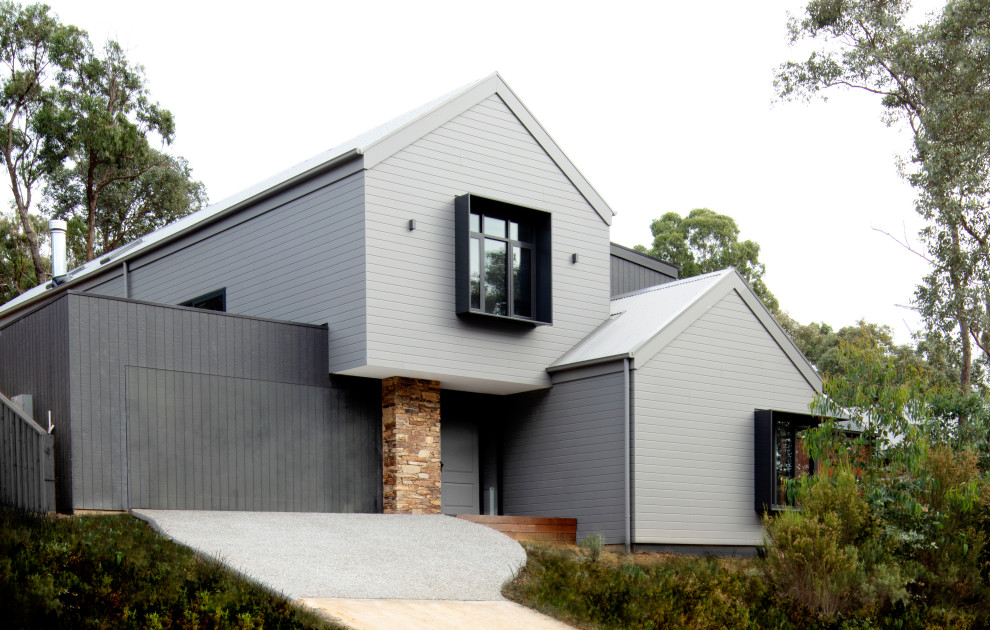 This is an example of a large contemporary two-storey grey house exterior in Melbourne with stone veneer, a gable roof and a metal roof.
