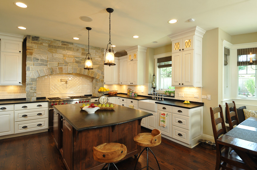 Mountain style l-shaped eat-in kitchen photo in Chicago with a farmhouse sink, raised-panel cabinets, white cabinets, soapstone countertops, white backsplash, subway tile backsplash and paneled appliances