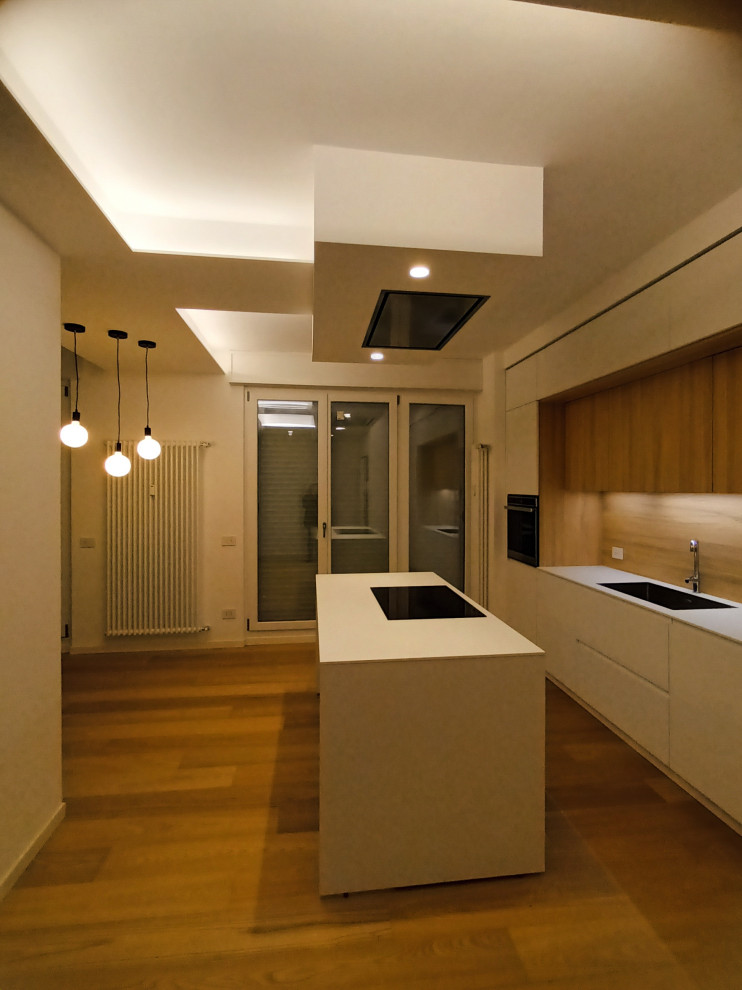 Design ideas for a small contemporary galley open plan kitchen in Milan with an integrated sink, flat-panel cabinets, white cabinets, multi-coloured splashback, wood splashback, black appliances, light hardwood flooring, an island, white worktops and a drop ceiling.
