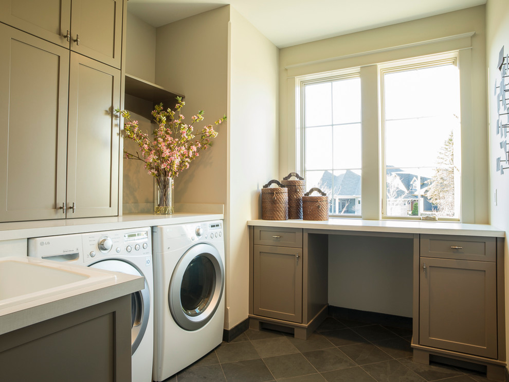 This is an example of a mid-sized transitional u-shaped laundry room in Minneapolis with a drop-in sink, flat-panel cabinets, grey cabinets, laminate benchtops, grey walls, slate floors and a side-by-side washer and dryer.
