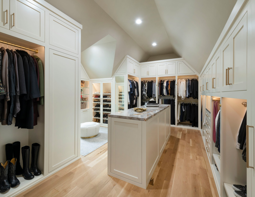 Modelo de armario vestidor unisex y abovedado grande con armarios estilo shaker, puertas de armario blancas, suelo de madera clara y suelo marrón