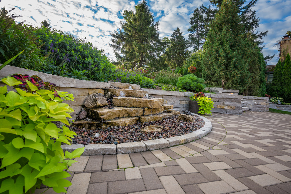 This is an example of a mid-sized traditional backyard patio in Milwaukee with a water feature, brick pavers and no cover.
