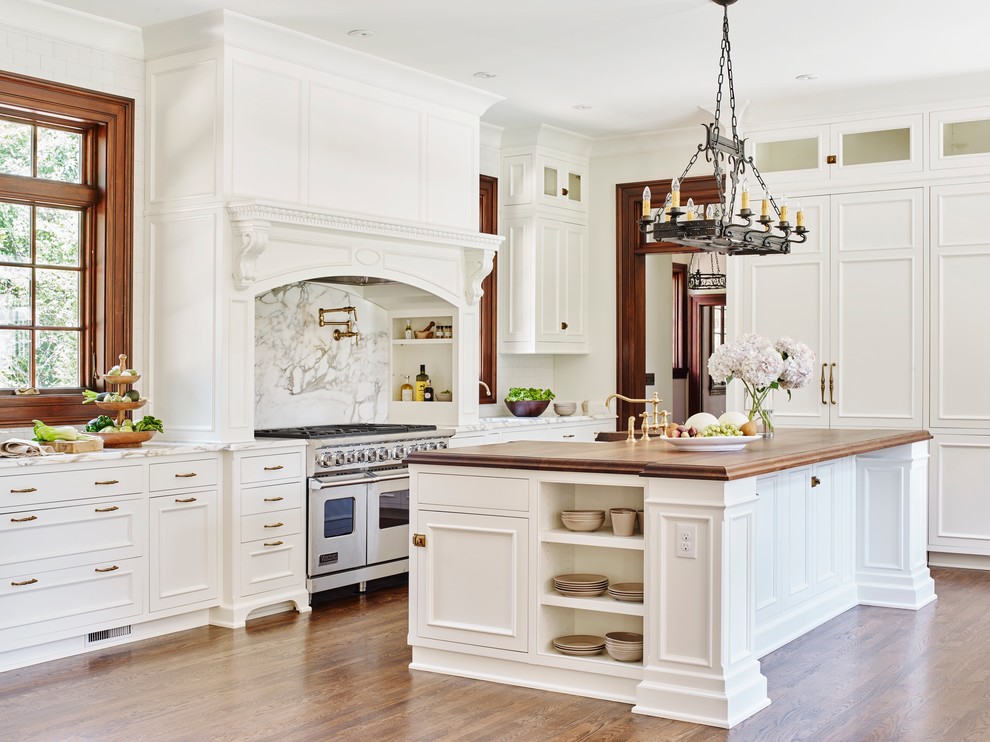 Elegant medium tone wood floor kitchen photo in Atlanta with a farmhouse sink, beaded inset cabinets, white cabinets, wood countertops, white backsplash, stone slab backsplash and an island