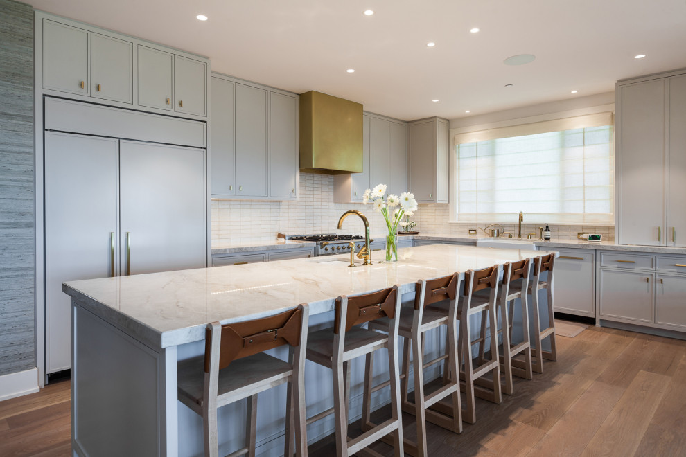 Kitchen - transitional l-shaped medium tone wood floor and brown floor kitchen idea in Seattle with a farmhouse sink, recessed-panel cabinets, gray cabinets, white backsplash, stainless steel appliances, an island and gray countertops