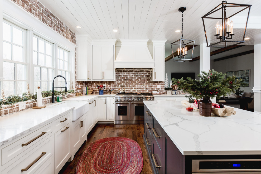 Inspiration for a large traditional u-shaped eat-in kitchen in DC Metro with a farmhouse sink, shaker cabinets, white cabinets, quartz benchtops, red splashback, brick splashback, stainless steel appliances, dark hardwood floors, with island, brown floor and white benchtop.