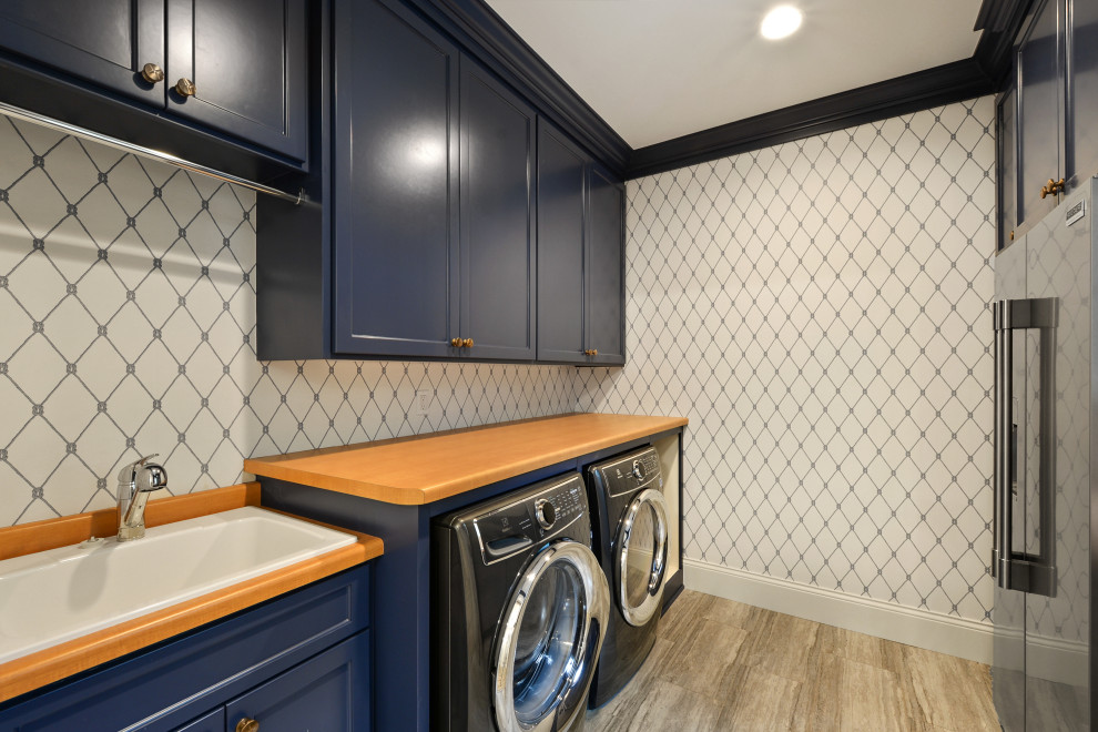 Multifunktionaler Hauswirtschaftsraum mit Ausgussbecken, blauen Schränken, bunten Wänden, Waschmaschine und Trockner nebeneinander, buntem Boden und beiger Arbeitsplatte in Minneapolis