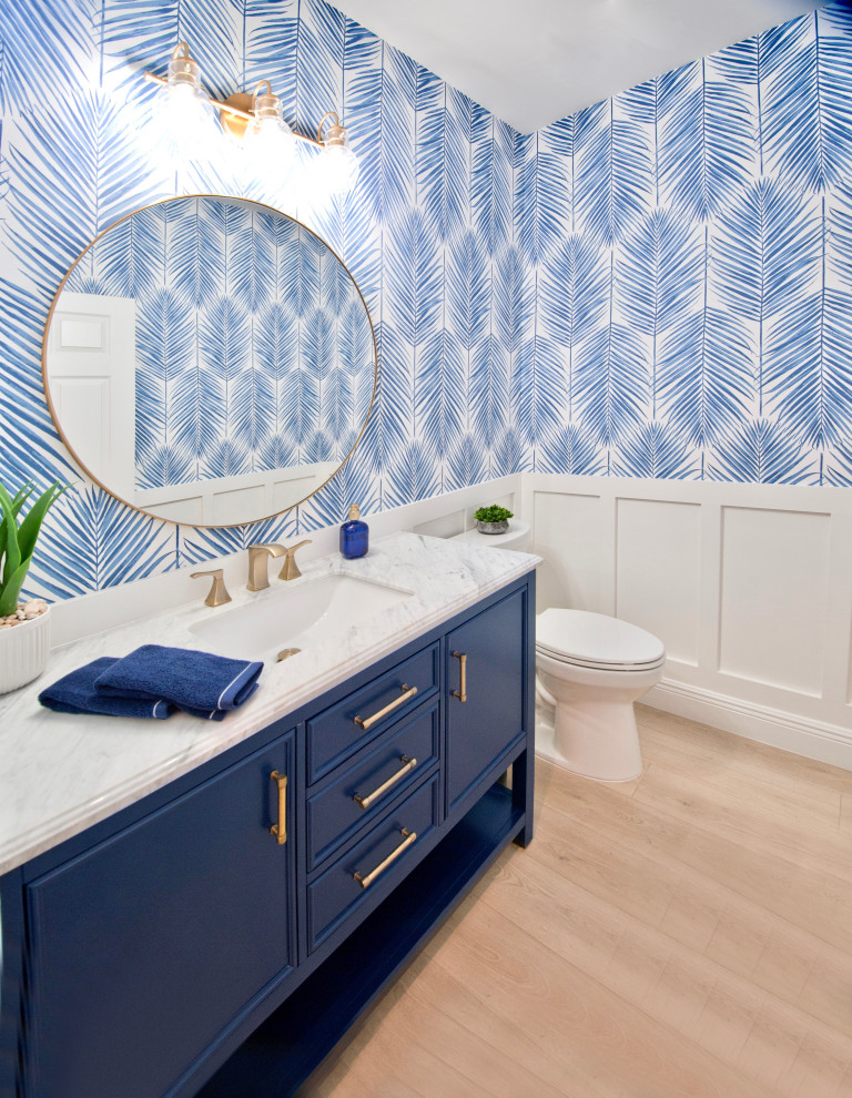 This is an example of a small beach style 3/4 bathroom in Miami with recessed-panel cabinets, blue cabinets, a two-piece toilet, blue walls, laminate floors, an undermount sink, marble benchtops, beige floor, white benchtops, a single vanity, a freestanding vanity and wallpaper.
