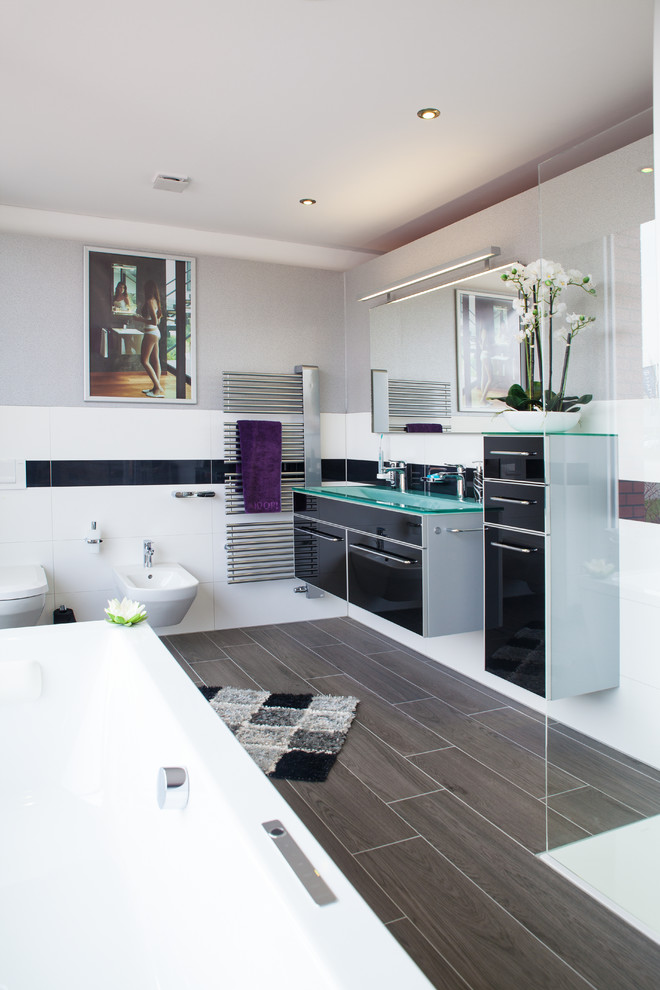 Inspiration for a mid-sized contemporary 3/4 wet room bathroom in Hamburg with flat-panel cabinets, black cabinets, a wall-mount toilet, black and white tile, ceramic tile, grey walls, an integrated sink, glass benchtops, brown floor, a hinged shower door and green benchtops.