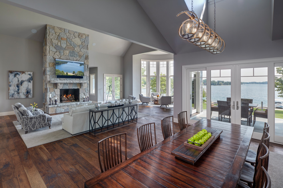 Inspiration for a large contemporary open plan dining room in Detroit with grey walls, dark hardwood flooring, a standard fireplace, a stacked stone fireplace surround, brown floors and a vaulted ceiling.