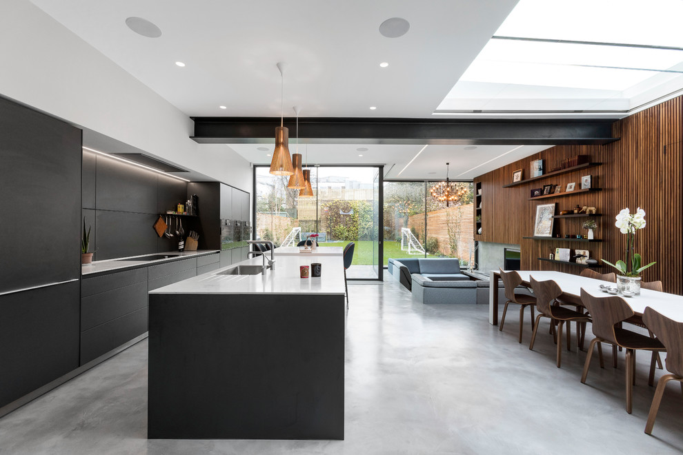 Contemporary galley kitchen in London with an undermount sink, flat-panel cabinets, black cabinets, panelled appliances, concrete floors, with island, grey floor and white benchtop.