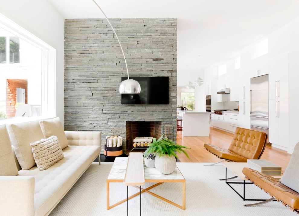 Inspiration for a contemporary open concept family room in New York with white walls, medium hardwood floors, a standard fireplace, a stone fireplace surround, a wall-mounted tv and beige floor.