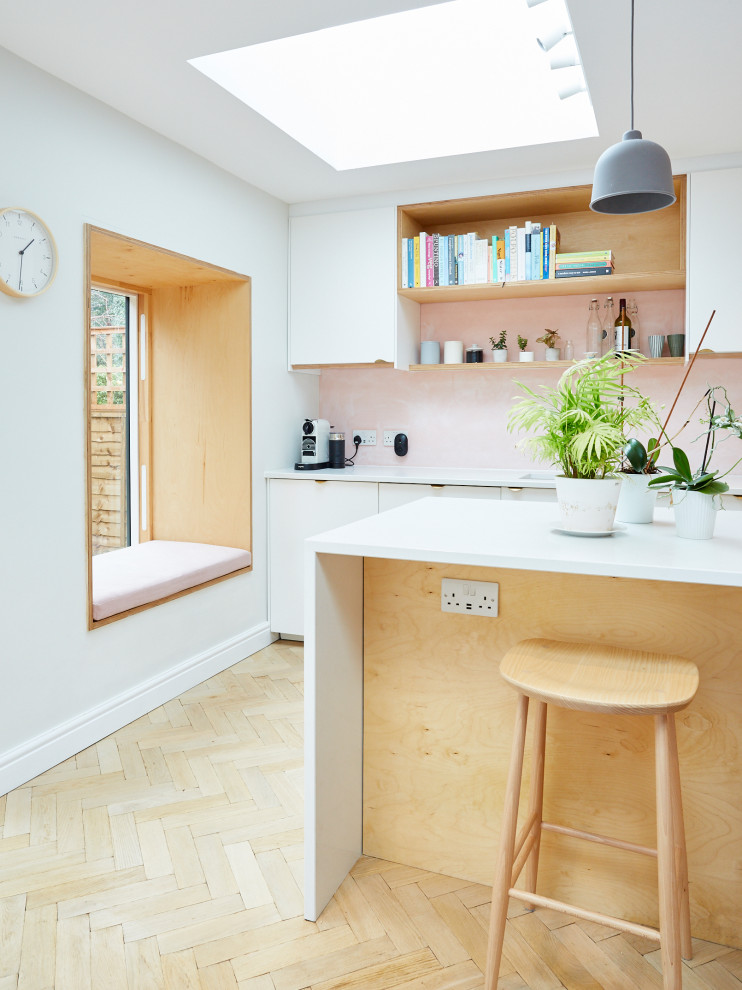 Photo of a medium sized contemporary grey and pink galley open plan kitchen in London with an integrated sink, flat-panel cabinets, white cabinets, quartz worktops, pink splashback, integrated appliances, light hardwood flooring, a breakfast bar, white worktops and feature lighting.