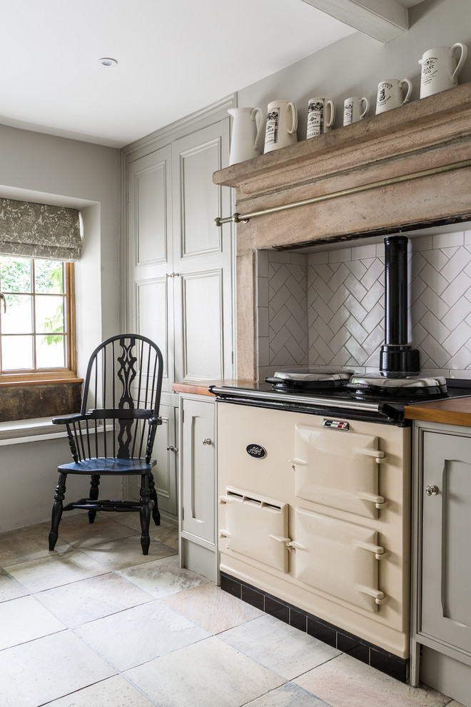 This is an example of a large country l-shaped eat-in kitchen in Other with a farmhouse sink, beaded inset cabinets, grey cabinets, wood benchtops, white splashback, ceramic splashback, panelled appliances, limestone floors, no island and multi-coloured floor.