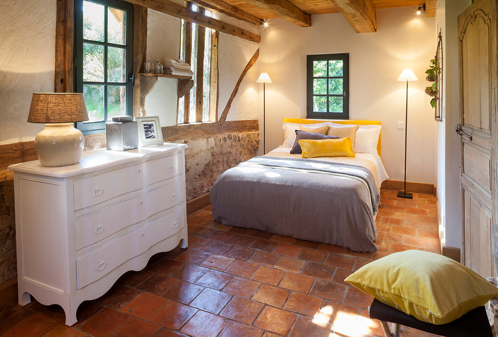 Design ideas for a mid-sized country guest bedroom in Other with white walls and terra-cotta floors.