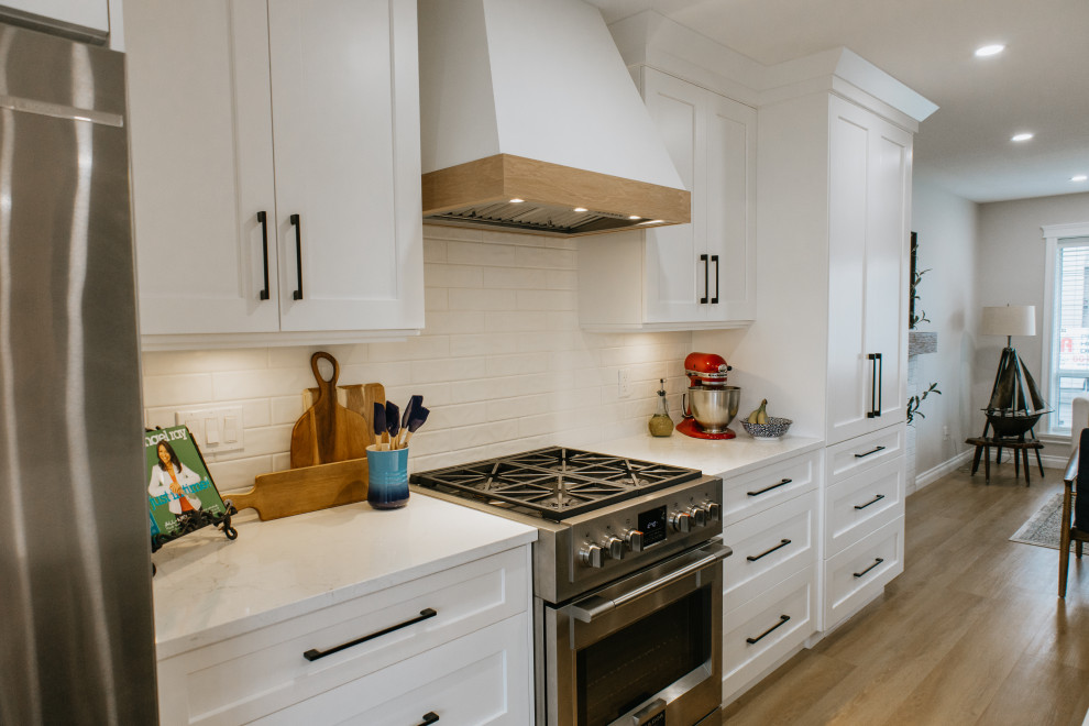Eat-in kitchen - large cottage single-wall vinyl floor eat-in kitchen idea in Vancouver with recessed-panel cabinets, white cabinets, an island, white countertops, an undermount sink, quartz countertops, white backsplash, porcelain backsplash and stainless steel appliances
