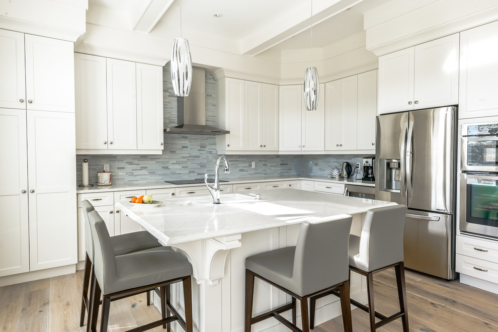 This is an example of a transitional l-shaped kitchen in Toronto with an undermount sink, shaker cabinets, white cabinets, blue splashback, matchstick tile splashback, stainless steel appliances, light hardwood floors and with island.