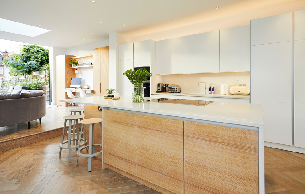Mid-sized contemporary single-wall open plan kitchen in London with an undermount sink, flat-panel cabinets, white cabinets, white splashback, stainless steel appliances, light hardwood floors, with island and beige floor.