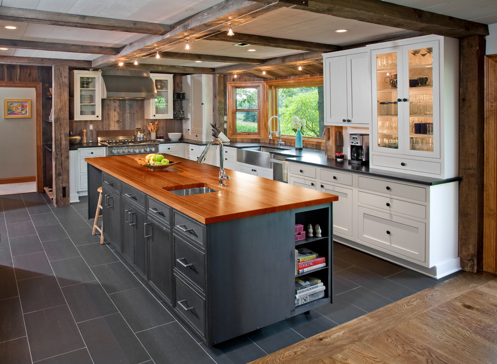 Industrial l-shaped kitchen in Philadelphia with a farmhouse sink, glass-front cabinets, white cabinets, wood benchtops, brown splashback, timber splashback, stainless steel appliances, with island and grey floor.