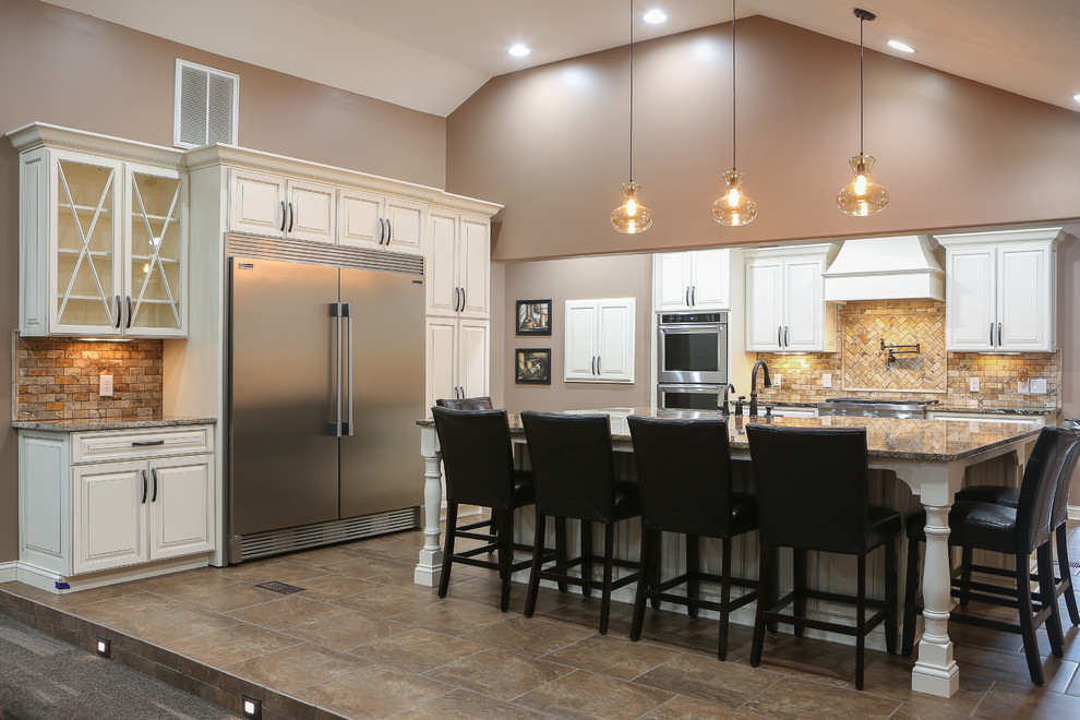 Open concept kitchen - large transitional u-shaped porcelain tile and brown floor open concept kitchen idea with a farmhouse sink, raised-panel cabinets, white cabinets, granite countertops, beige backsplash, travertine backsplash, stainless steel appliances and an island